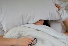 피로를 극복하는 에너지 보충법 person lying on bed while covering face with pillow and holding eyeglasses