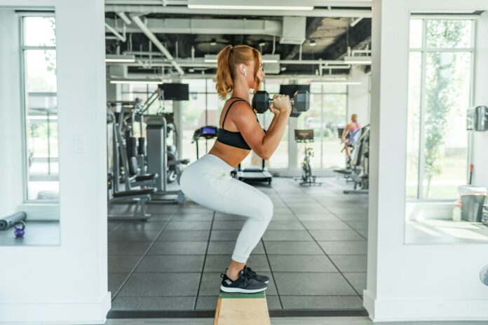 Photo by Benjamin Klaver woman wearing black sports bra and white legging lifting dummbells