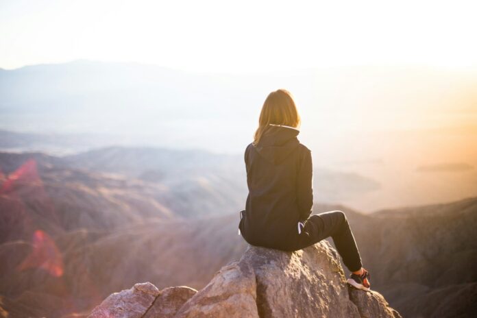 Photo by Denys Nevozhai person sitting on top of gray rock overlooking mountain during daytime