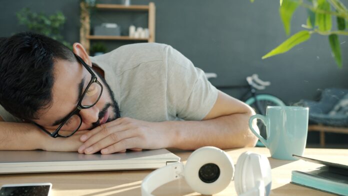 Photo by Vitaly Gariev Man sleeping at desk with headphones and coffee.